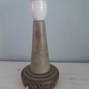 May include: A ceramic table lamp with a brown and green base and a white lampshade. The base has a textured surface and a carved design.