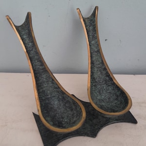 Peut inclure: Deux sculptures abstraites en bronze. Chacune a une forme de goutte d'eau avec un bord doré et un sommet fourchu. Les deux sculptures sont reliées par une base vert foncé avec un bord décoratif.