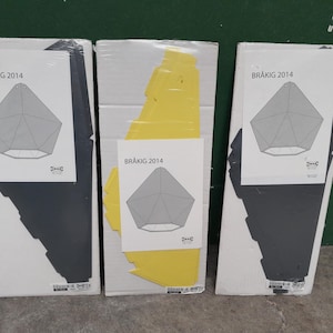 May include: Three boxes of IKEA BRÅKIG 2014 pendant lamps. Each box has a white background with a gray geometric design and a diagram of the lamp. One box has a yellow interior, the others have gray interiors.