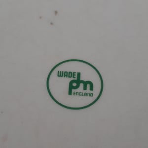 May include: A close-up of a white surface with a green circular logo. The logo features the words "WADE" and "pm" in a stylized font, with "ENGLAND" below. The logo is enclosed in a green circle.