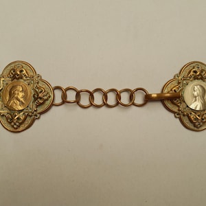 May include: An antique gold-toned metal clasp with a chain of small rings. Each end features a quatrefoil design with a central medallion. One medallion depicts a profile, the other a bust.
