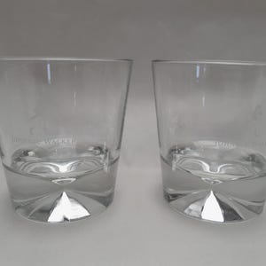 Pu&ograve; includere: Due bicchieri da whisky bassi e trasparenti. Ogni bicchiere ha una base spessa e geometrica e un bordo leggermente angolato. Il testo "JOHNNIE WALKER" &egrave; stampato sulla parte anteriore di ogni bicchiere. I bicchieri sono vuoti.