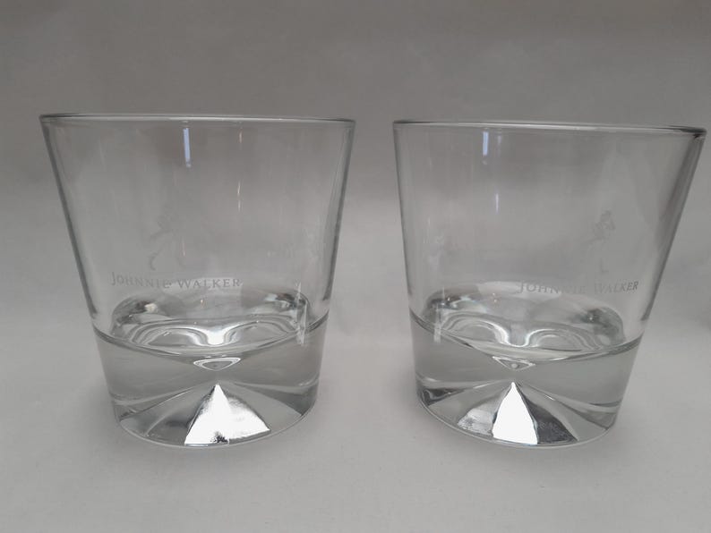 Pu&ograve; includere: Due bicchieri da whisky bassi e trasparenti. Ogni bicchiere ha una base spessa e geometrica e un bordo leggermente angolato. Il testo "JOHNNIE WALKER" &egrave; stampato sulla parte anteriore di ogni bicchiere. I bicchieri sono vuoti.