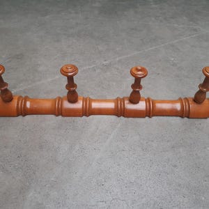 Op de afbeelding: Een houten kapstok met vier gedraaide haken. De kapstok heeft een warme, bruine kleur en een decoratief, gedraaid ontwerp. De haken zijn ook gedraaid en hebben een afgeronde bovenkant. De kapstok is ontworpen om aan de muur te worden bevestigd.