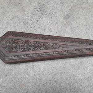 Può includere: Una scatola di legno marrone scuro con intagli intricati. La scatola è a forma di bara e ha un coperchio.