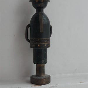 May include: A small, black and gold figurine of a person wearing a helmet. The figurine is standing on a base.