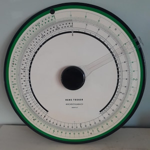 Może przedstawiać: Okrągła suwmiarka z białym środkiem, czarnymi i zielonymi pierścieniami zewnętrznymi oraz przezroczystym plastikowym ramieniem. Na powierzchni wydrukowano tekst "HANS TRÖGER KIRCHENTHUMBACH". Narzędzie do obliczeń matematycznych.