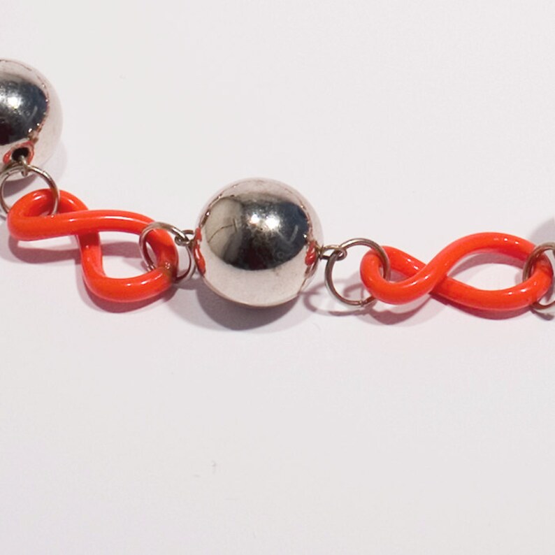 May include: A silver and orange beaded necklace with a repeating pattern of silver balls and orange infinity symbols.