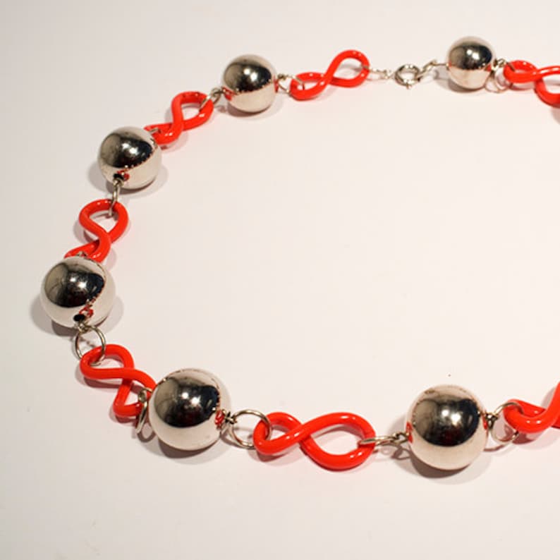 May include: A necklace with silver balls and bright orange infinity symbol links.