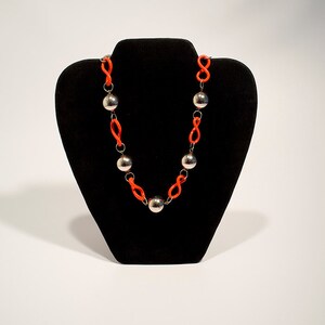 May include: A necklace with a silver chain and orange beads. The necklace is displayed on a black velvet stand.