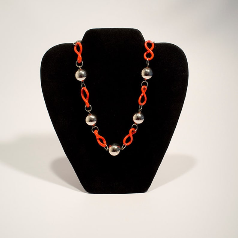 May include: A necklace with a silver chain and orange beads. The necklace is displayed on a black velvet stand.