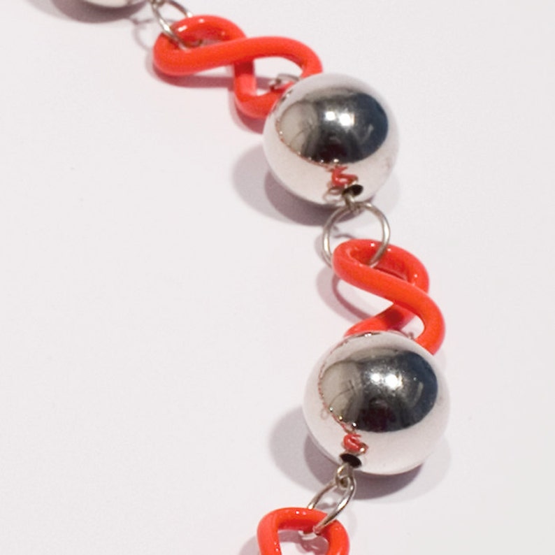 May include: A silver necklace with orange beads and silver balls. The beads are shaped like a figure eight.