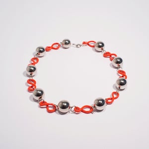 May include: A silver and orange necklace with round silver beads and orange links. The necklace is made of metal and plastic.