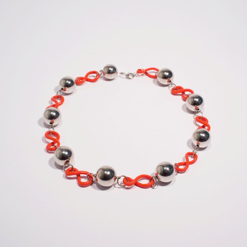 May include: A silver and orange necklace with round silver beads and orange links. The necklace is made of metal and plastic.