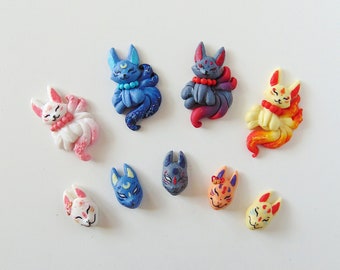 Op de afbeelding: Negen kleurrijke kitsune-figuurtjes, elk met een ander kleurenschema en ontwerp. De figuurtjes zijn gemaakt van polymer clay en hebben ingewikkelde details, waaronder gezichtsuitdrukkingen, vacht en staarten.