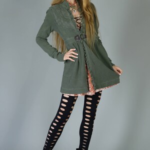 May include: A woman wearing a green, lace-trimmed cardigan with a brown belt, black fishnet tights, and black ankle boots.