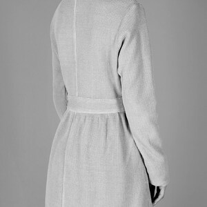 May include: A long-sleeved, gray waffle knit cardigan with a belt. The cardigan has a V-neck and a slightly flared hem.