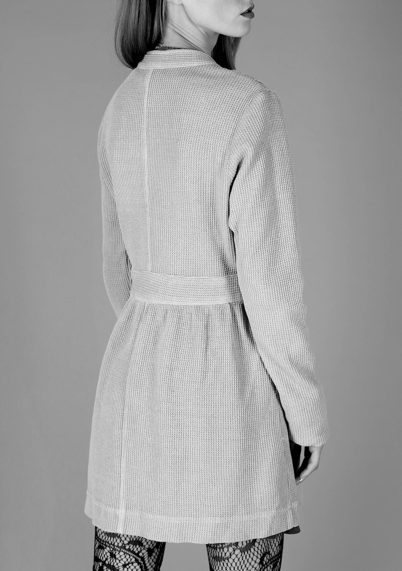 May include: A long-sleeved, gray waffle knit cardigan with a belt. The cardigan has a V-neck and a slightly flared hem.
