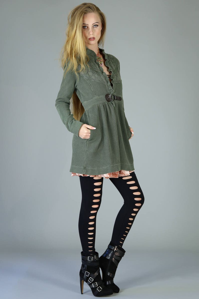 May include: A woman wearing a green, long-sleeved, collared dress with a brown belt and black tights with cutouts. She is wearing black heeled boots with buckles.