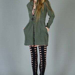 May include: A woman wearing a green jacket with a belt, black tights with cutouts, and black heeled boots.