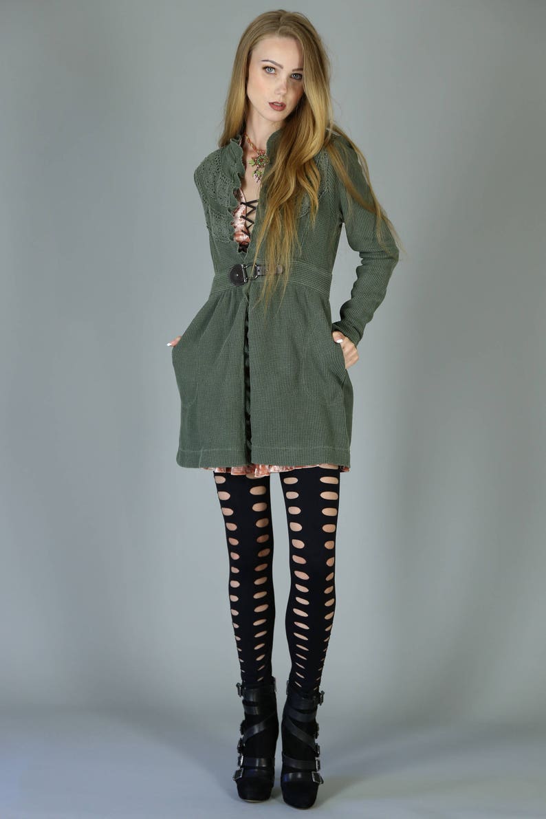May include: A woman wearing a green jacket with a belt, black tights with cutouts, and black heeled boots.