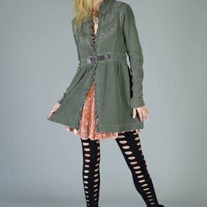 May include: A woman wearing a green, lace-trimmed jacket with a brown belt, a pink velvet skirt, black fishnet tights, and black heeled boots.