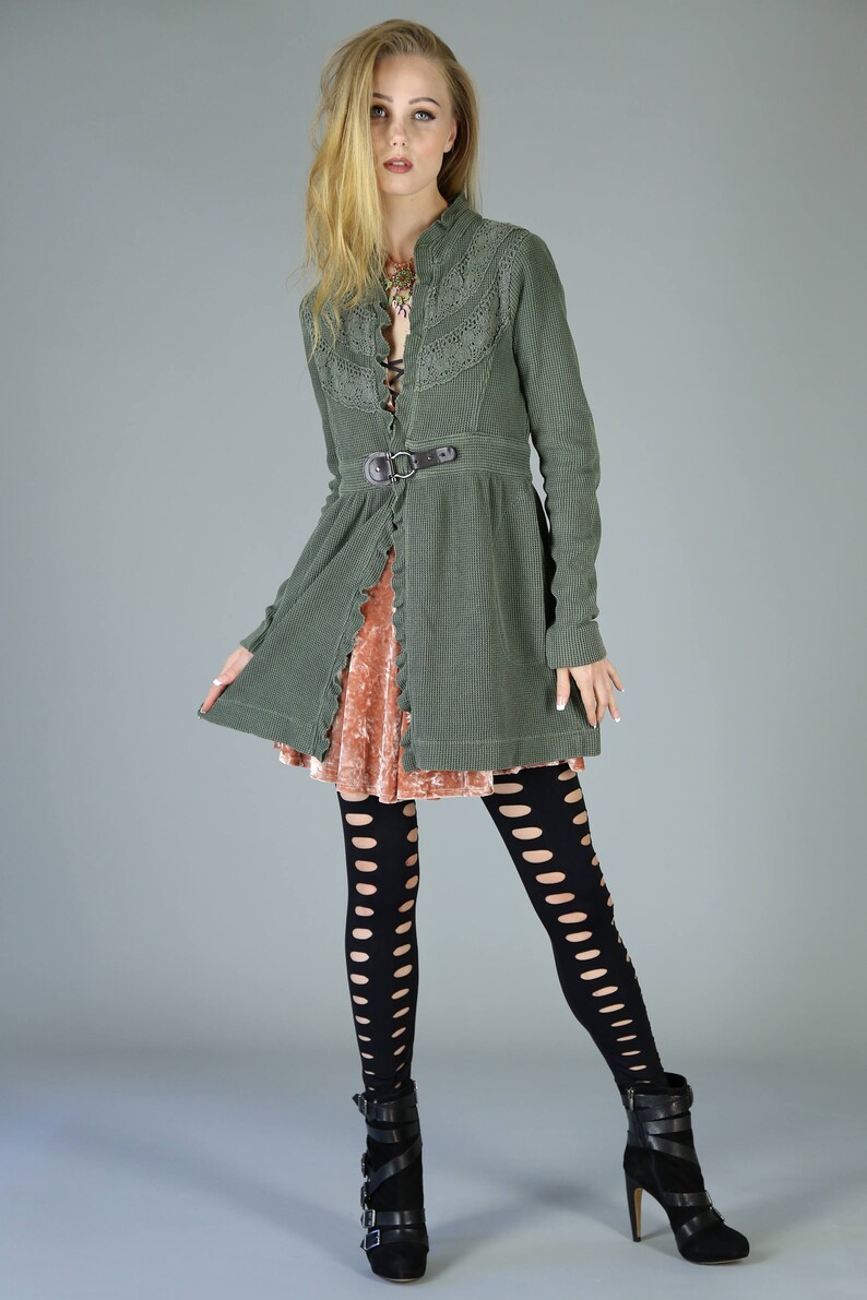 May include: A woman wearing a green, lace-trimmed jacket with a brown belt, a pink velvet skirt, black fishnet tights, and black heeled boots.