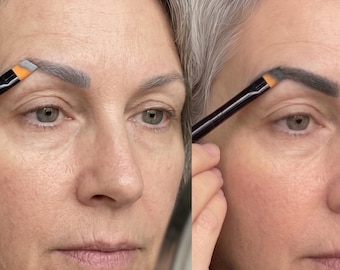 May include: A woman's face with gray hair and fair skin. A black makeup brush with an orange tip is used to apply eyebrow makeup. The before and after application of the eyebrow makeup is shown.