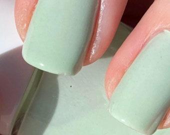 Peut inclure: Gros plan sur des ongles peints avec un vernis à ongles vert clair. Les ongles sont courts et de forme ovale.