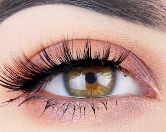 May include: Close-up of a human eye with long, dark eyelashes and brown iris. The eye is open and looking directly at the camera. The eyelid is lightly shaded with a peachy-pink eyeshadow.
