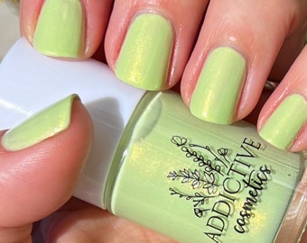 Puede incluir: Una botella de esmalte de uñas verde claro con un acabado brillante. La botella está etiquetada con "ADDICTIVE cosmetics".