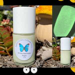 May include: A small bottle of light green nail polish with a white cap. The bottle has a label that says "Addictive Cosmetics" and "10 Free Nail Polish Vegan". The polish glows green in the dark.