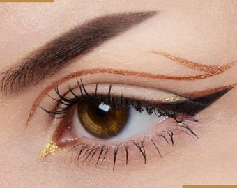 May include: Close-up of an eye with gold and brown eyeliner. The eyeliner is in a curved, abstract design.