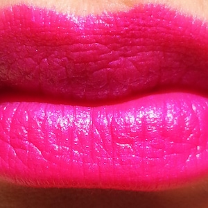 Pu&ograve; includere: Primo piano di labbra coperte da rossetto rosa acceso. Il rossetto ha una finitura lucida, che mette in risalto la consistenza delle labbra. Il colore &egrave; una tonalit&agrave; di rosa vibrante e satura.