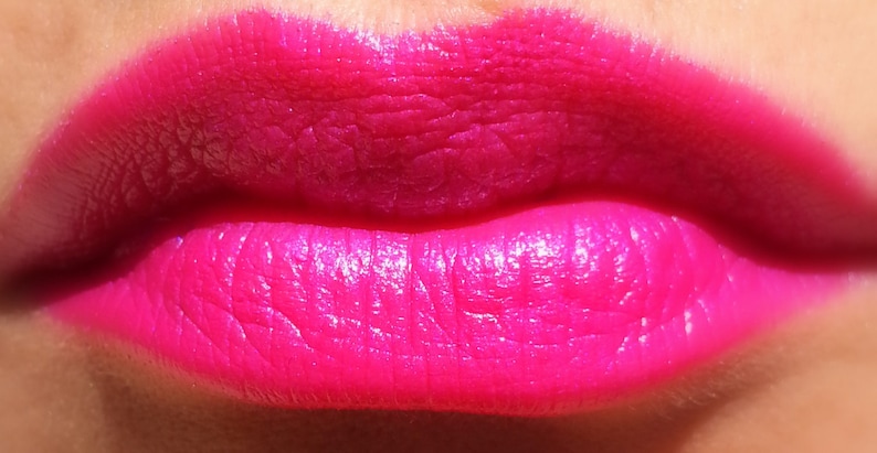 Pu&ograve; includere: Primo piano di labbra coperte da rossetto rosa acceso. Il rossetto ha una finitura lucida, che mette in risalto la consistenza delle labbra. Il colore &egrave; una tonalit&agrave; di rosa vibrante e satura.