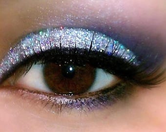 May include: Close-up of a woman's eye with silver glitter eyeshadow and black eyeliner. The eye is looking directly at the camera.
