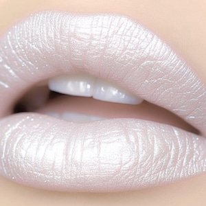May include: Close-up of a person's lips coated in pearlescent, shimmering white lipstick. The lips are full and well-defined, with a glossy finish. The teeth are white and visible. The overall effect is glamorous and eye-catching, perfect for a makeup or beauty product listing.