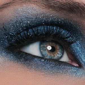 May include: Close-up of a blue eye with glitter eyeshadow and long black eyelashes.
