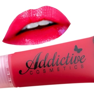 Könnte beinhalten: Ein rosa Lipgloss-Röhrchen mit einem schwarzen Etikett, auf dem "Addictive Cosmetics" und ein Schmetterlingsdesign stehen. Der Lipgloss ist leuchtend rosa.