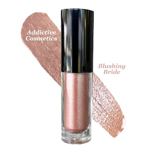 Könnte beinhalten: Eine transparente Glasröhre mit schimmerndem, roségoldenem flüssigen Lidschatten und schwarzem Deckel. Die Texte "Addictive Cosmetics" und "Blushing Bride" sind auf dem Bild zu sehen. Ein Farbmuster der gleichen Farbe wird gezeigt.