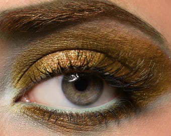 May include: Close-up of a woman's eye with gold eyeshadow and long eyelashes. The eyeshadow has a shimmery finish and is applied to the entire eyelid.