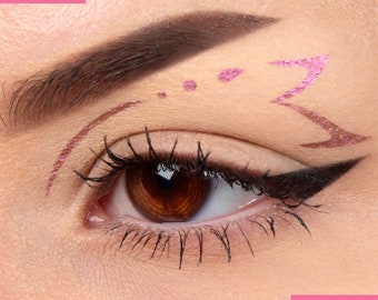 May include: Close-up of a woman's eye with a dramatic winged eyeliner look. The eye is adorned with a pink and brown glitter design above the crease.