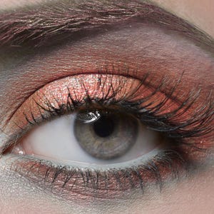 May include: Close-up of a woman's eye with shimmery peach eyeshadow and long, dark eyelashes.