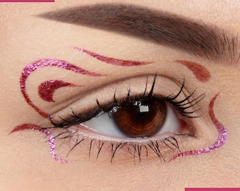 May include: Close-up of an eye with a pink and brown glitter eyeliner design. The eyeliner is in a swirling pattern around the eye.
