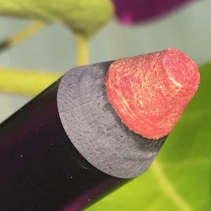 May include: Close-up of a pink and silver lip liner pencil. The pencil is sharpened and ready to use.