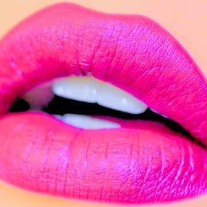 Pu&ograve; includere: Primo piano di un paio di labbra dipinte con rossetto rosa brillante. Le labbra sono leggermente socchiuse, rivelando denti bianchi contro uno spazio nero. Lo sfondo &egrave; di un colore pesca tenue.