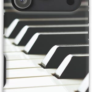 May include: Close-up of a phone case featuring a piano keyboard design. The case has a black camera module with three lenses. The piano keys are black and white, creating a classic musical aesthetic.