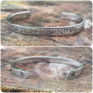 May include: A silver bangle bracelet with a Norse inscription and a triple spiral design on the ends. The inscription reads "SNIM DXXMFDXM".