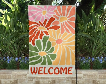 May include: A welcome garden flag with a retro design featuring colorful stylized flowers in shades of pink, orange, green, and yellow. The flag has the word "WELCOME" printed in bold red letters at the bottom.