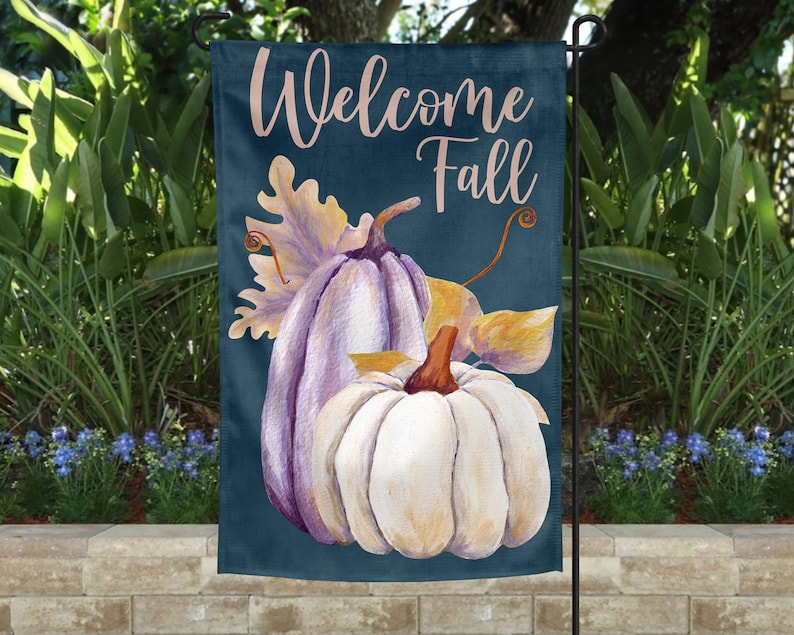May include: Welcome Fall garden flag with a blue background and two pumpkins. The pumpkins are painted white and purple with a yellow leaf behind them.